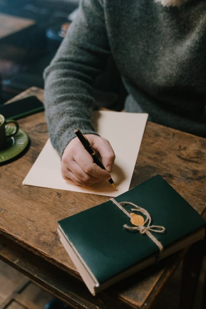 Adult writing on paper at wooden table, capturing a cozy and focused atmosphere.